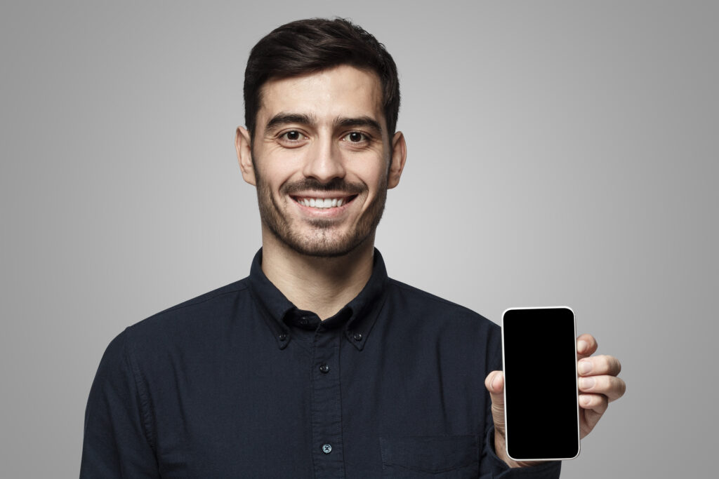 Close-up portrait of smiling man looking at camera, holding phone with blank screen